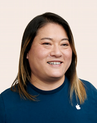 Apple Retail employee with shoulder-length hair, smiling at the camera.