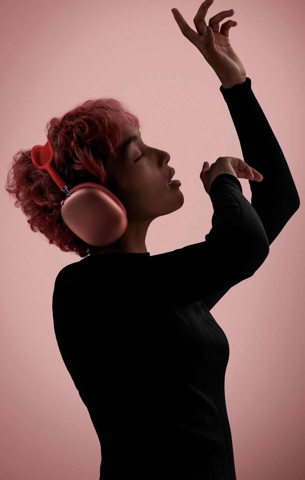 Side profile of person in motion with eyes closed and arms raised wearing AirPods Max in pink.