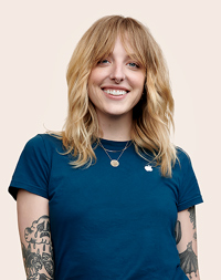 Apple Retail employee with arm tattoos, smiling at the camera.