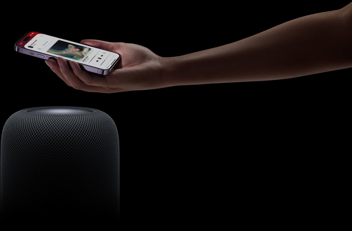 A hand coming in from the right side of the page holds an iPhone above a スロット シアター 四海 樓 データ HomePod speaker