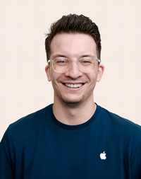 Apple Retail employee with short, dark hair, smiling at the camera. 